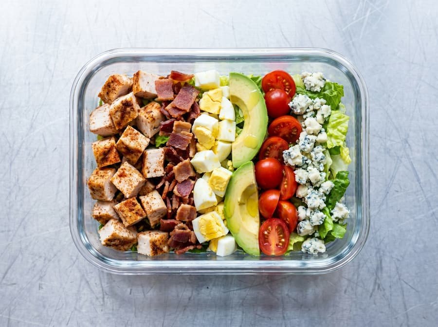 Cobb Salad with rows of chicken, egg, bacon, avocado and tomato over greens